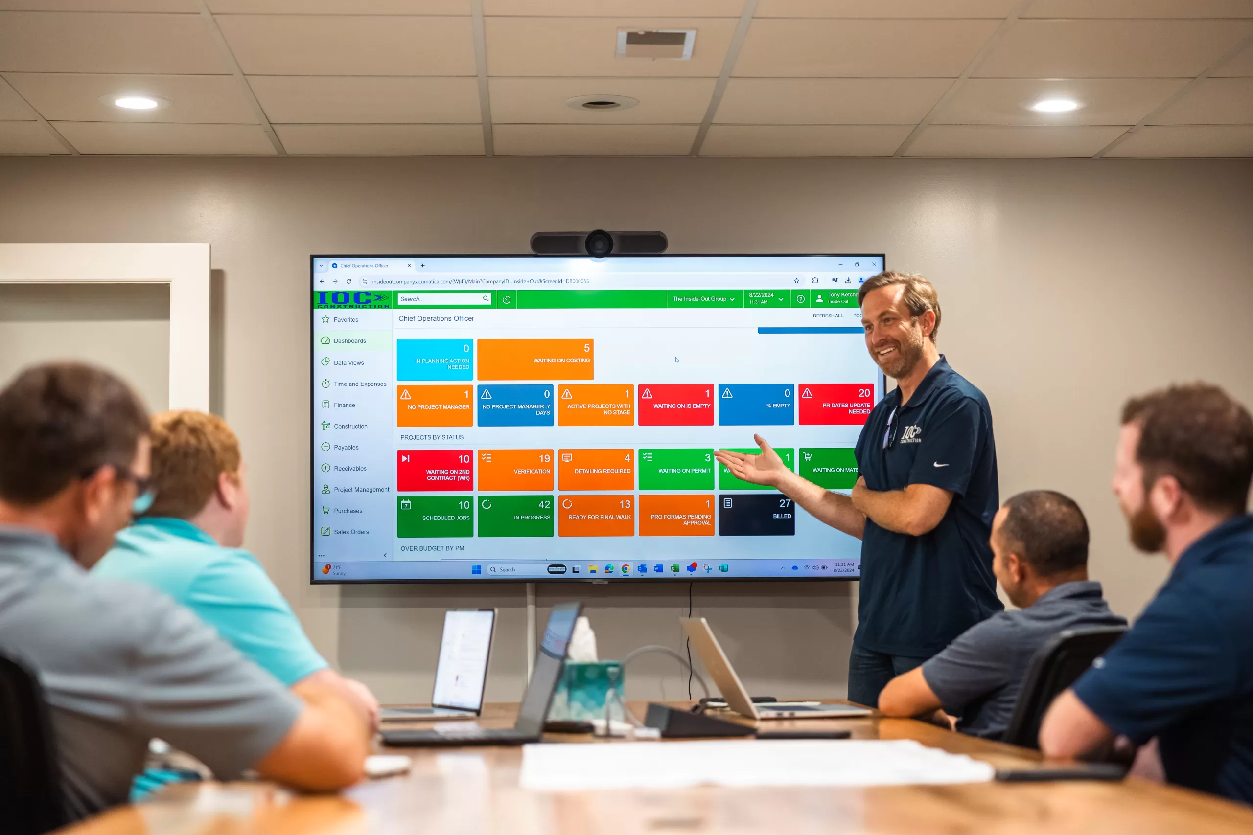 Construction project meeting with team reviewing digital plans and scheduling on screen.
